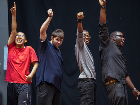 Four young disabled men raise their fists in the air in solidarity