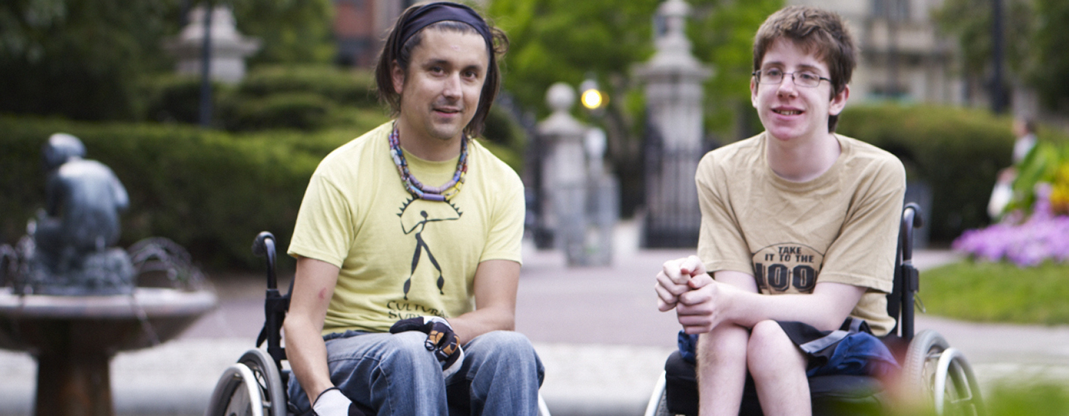 Two men using wheelchairs and wearing yellow shirts visiting the Boston Public Garden
