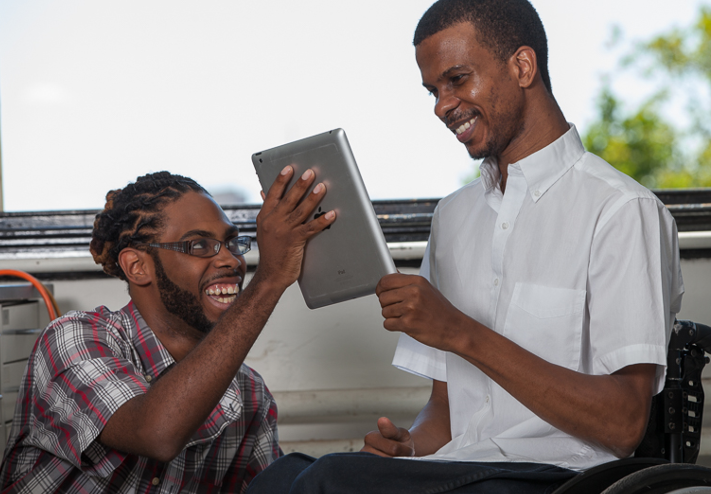 Two young black men looking at an iPad screen, smiling at what they see