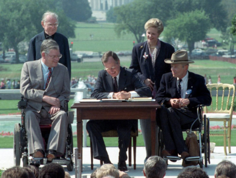 George H.W. Bush signs the ADA into law, with two disabled advocates and lawmakers seated next to him in their wheelchairs