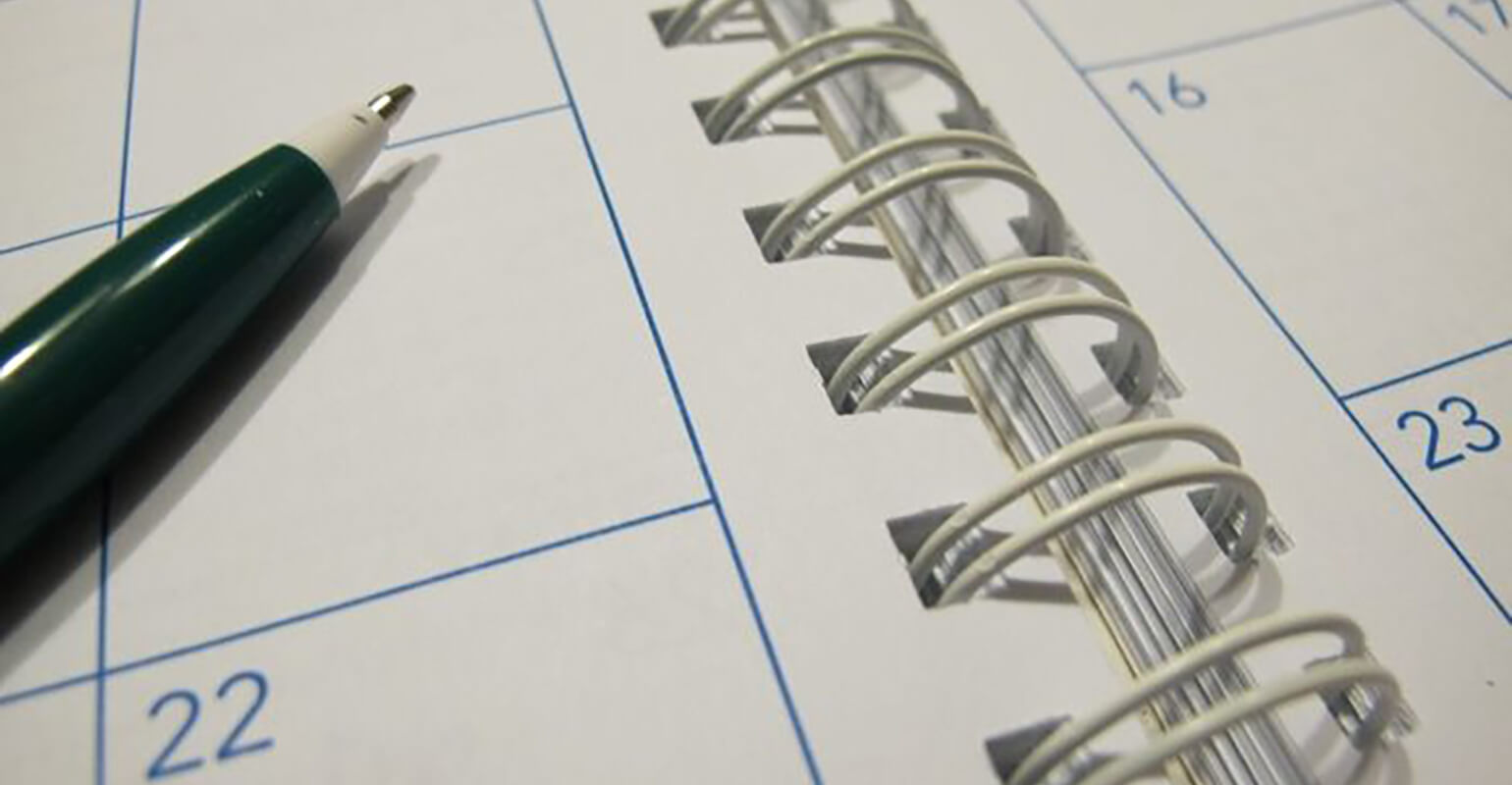 An image of a spiral bound calendar, there is a green pen laid across the left page.
