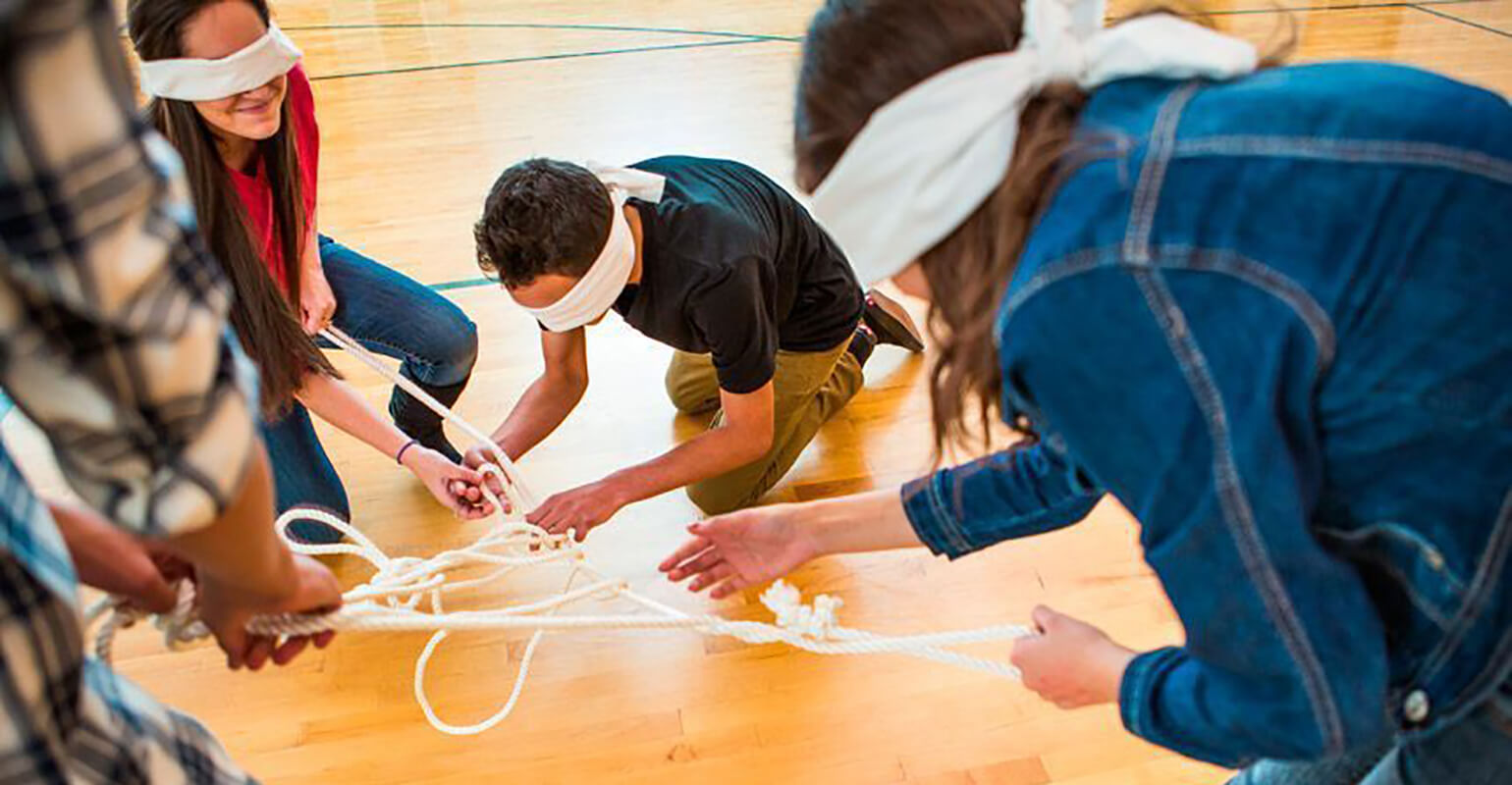 A group of young adults working together to untie the knot in a rope while blindfolded.