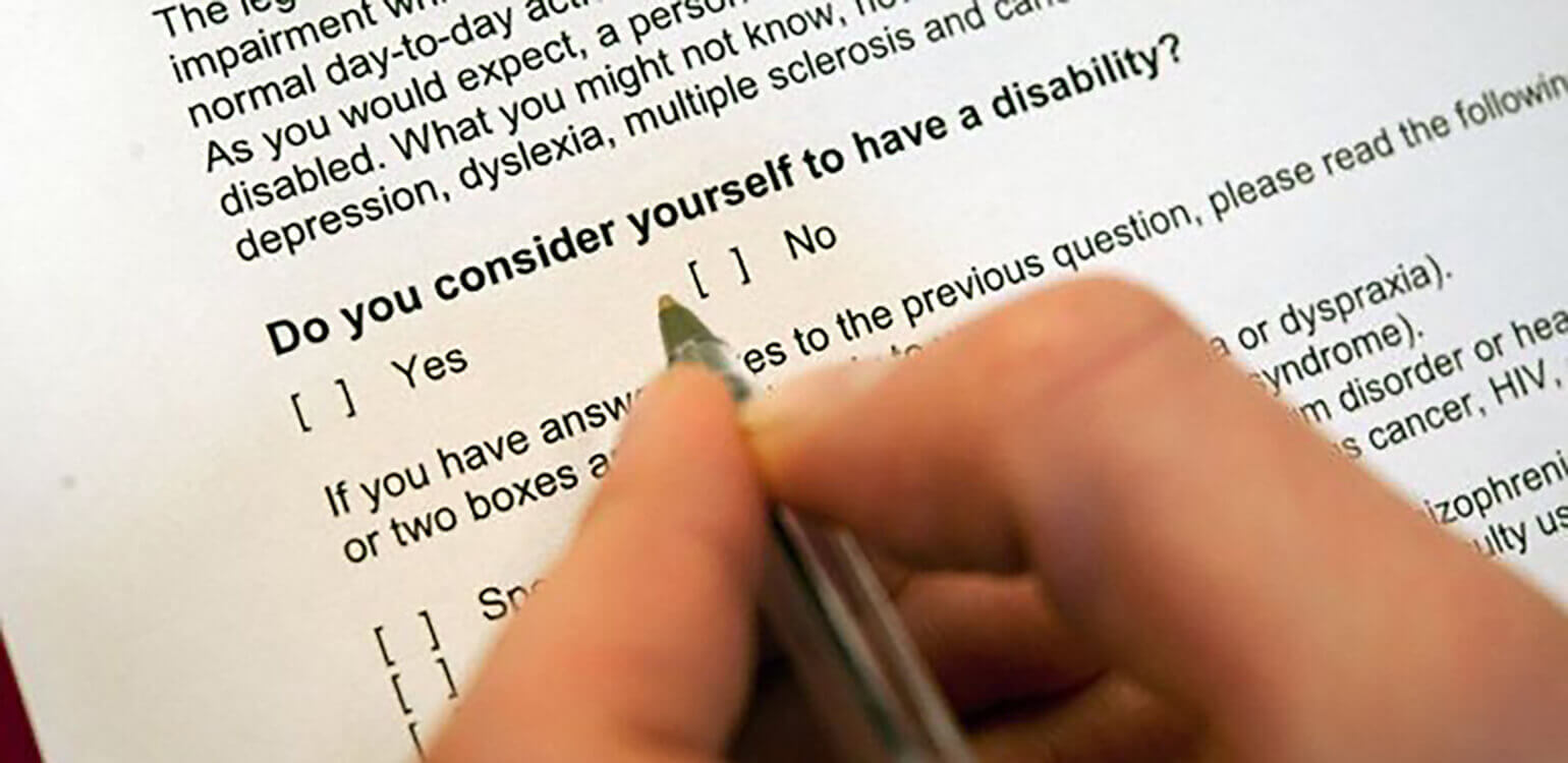 An image of a person filling out an application. On the application there is the question: 'Do you consider yourself to have a disability?' There is an option to check yes or no.