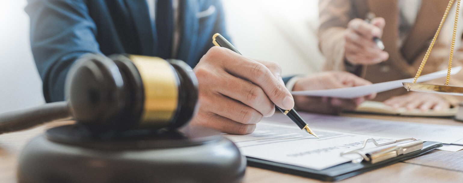An image of a person writing on a clipboard. The person has a scale and gavel on their desk to indicate that they are a lawyer.