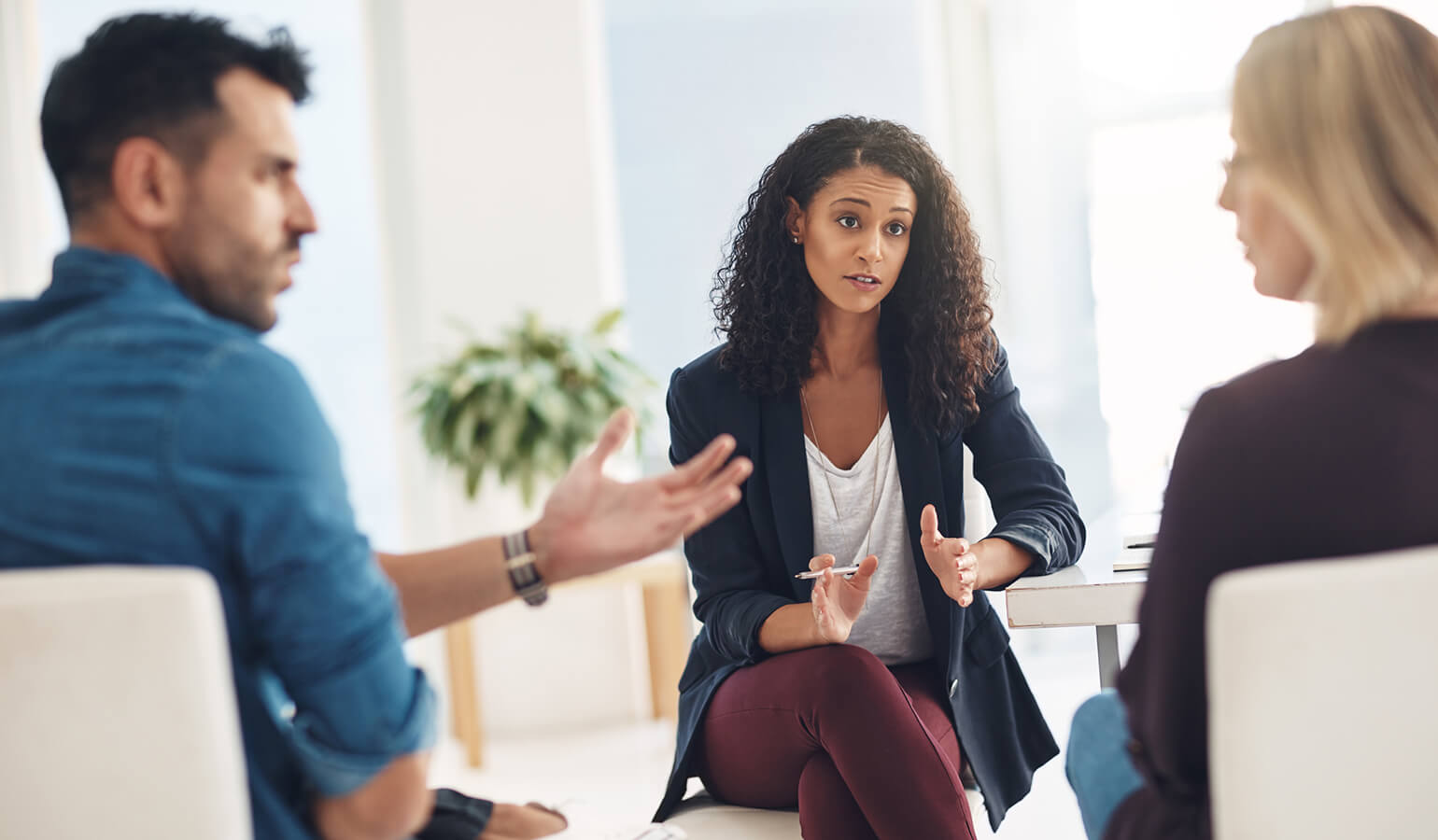An image of a mediation session. There are three people sitting in a circle. Two of the people seem to be speaking emotionally to each other. The third person is listening to them and looks to be responding.