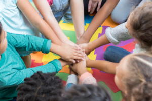 Color photo of children's hands clasped together in a huddle representing teamwork and friendship.